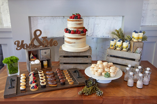 A rustic dessert table for a party or wedding featuring a cake, macaroons, tarts and chocolate milk.