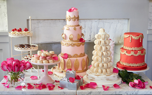 An elegant dessert table for a party or wedding featuring ornate cakes, macaroon tree, tarts wedding favors and rose petals.