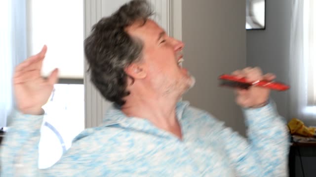 Mature man singing into a hairbrush in his living room having the time of his life