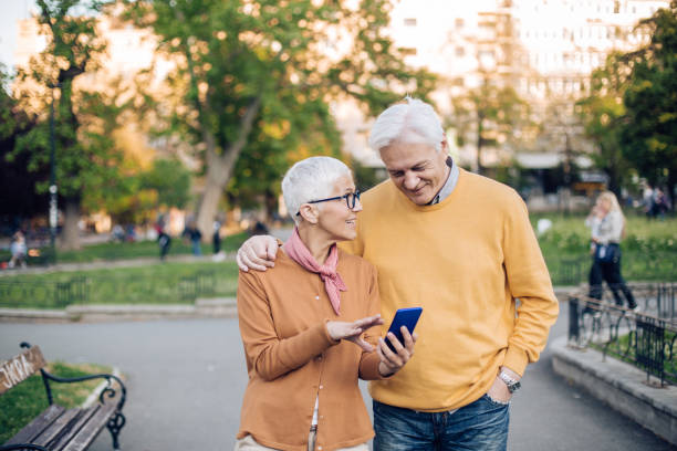 istock Cheerful old couple walking around a public park, using a smart phone 1225882088