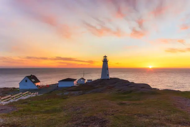 Photo of Beautiful sunrise over a white lighthouse sitting at the edge of a rocky cliff.