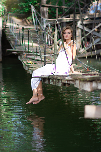 Young woman waving her feet from the old bridge over the river. time to relax