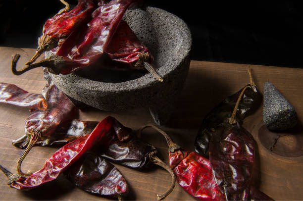 Guajillo Dry Peppers and molcajete, Concept of Mexican Food Ingredients Chile Guajillo on a molcajete and on a wooden table in a low light environment or low key light, ingredient to prepare salsa as part of Mexican food. Still life food. chile photos stock pictures, royalty-free photos & images
