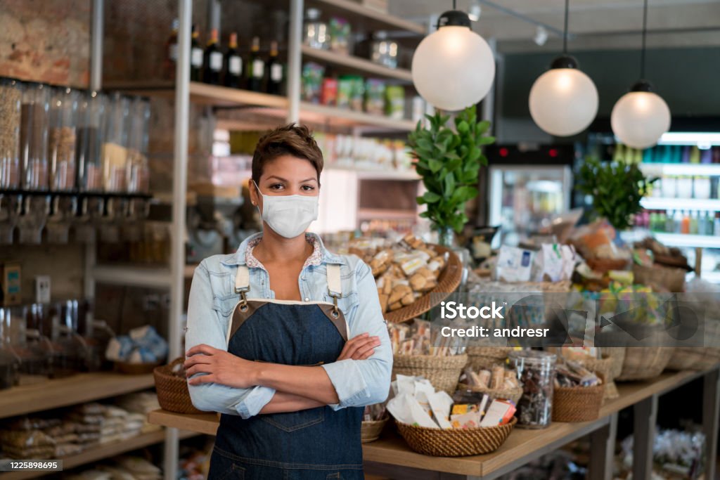 Geschäftsinhaber arbeitet in einem Lebensmittelgeschäft mit einer Gesichtsmaske - Lizenzfrei Speisen Stock-Foto