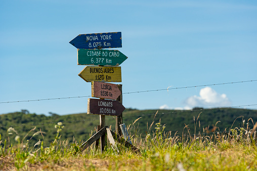 Tourist mountain path through green plants and cloudy fog with a wooden destination sign