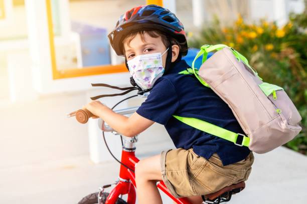 little boy riding a bicycle wearing a protective mask - little boys preschooler back to school backpack imagens e fotografias de stock