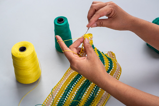 a woman making a thread pattern with yellow and green threads using crochet hook