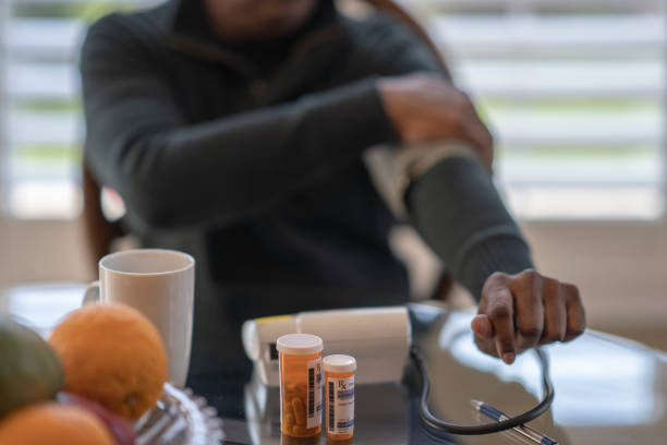 West Indian man checks his blood pressure at home Mature man uses a home medical device to check his blood pressure while sitting at his kitchen table. blood pressure medication stock pictures, royalty-free photos & images
