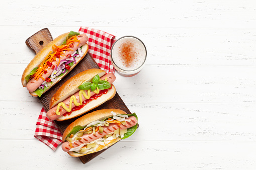 Various hot dog with vegetables, lettuce and condiments and beer glass on wooden background. Top view with copy space. Flat lay
