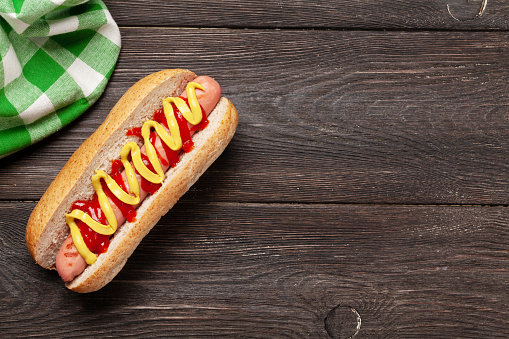 Hot dog with mustard and ketchup on wooden background. Top view with copy space. Flat lay
