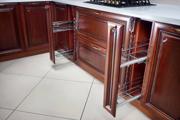 istock Pull out spice rack cabinet filler pantry. Two vertical drawers for spices shelf under countertop with wooden panel. Classic style interior kitchen with golden elements cherry alder wood cabinetry. 1225927699