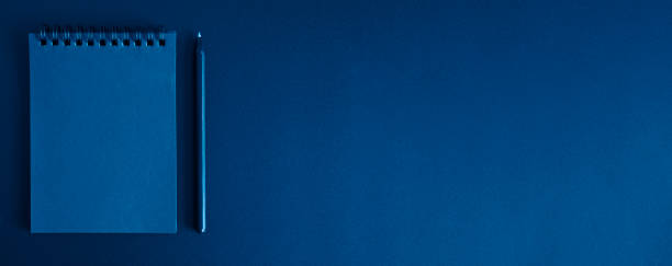 istock notebook on a spring and a pen on a black background. space for text. banner. toned classic blue color 1225927935