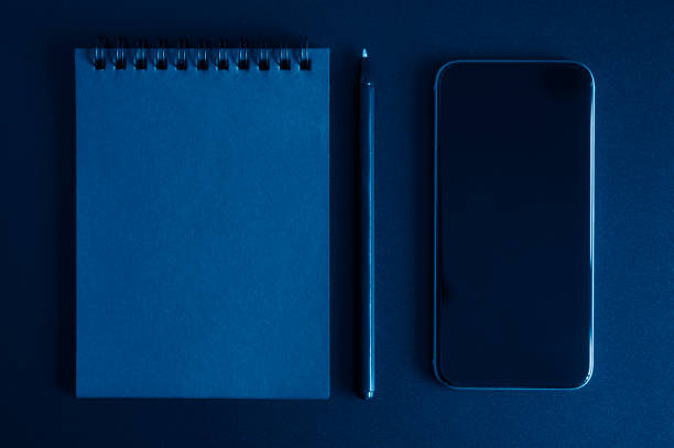 istock notebook on a spring, and a pen, and mobile phone on a black background. space for text. toned classic blue color 1225928857