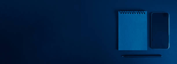 istock notebook on a spring, and a pen, and mobile phone on a black background. space for text. banner. toned classic blue color 1225929002