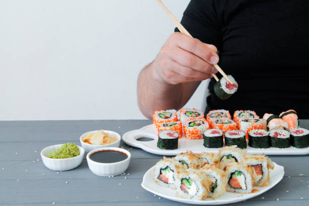 istock Man eating sushi set with chopsticks in restaurant with copy space 1225930887