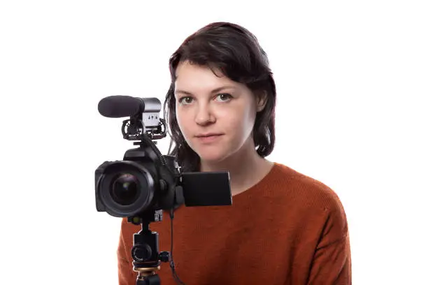 Female art student studying to be a filmmaker using a camera on a tripod for a project. She looks confident about her creativity. Depicts entertainment industry production and education