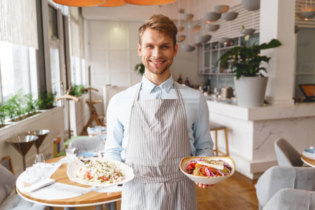 istock Cheerful male waiter holding two cooked dishes 1225932893