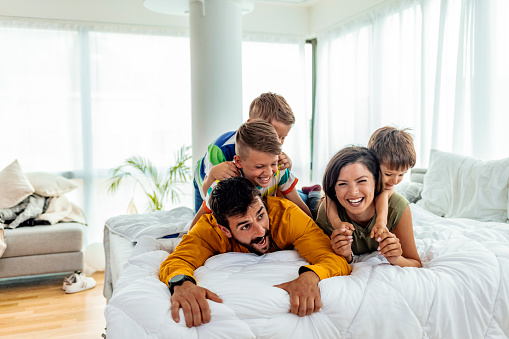Happy family relaxing on the sofa together at home. Happy family, mother, father and children laughing, playing and tickles in bed in bedroom at home.