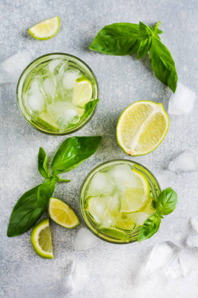 Summer homemade lemonade made from lime, lemon, cucumber and basil with ice in glass on an old concrete background. Selective focus. Summer homemade lemonade made from lime, lemon, cucumber and basil with ice in glass on an old concrete background. Selective focus. lime basil plant stock pictures, royalty-free photos & images