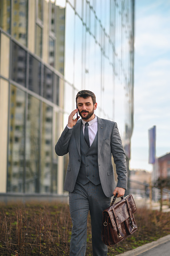 Handsome smiling business man walking down the street going to work and talking on the phone