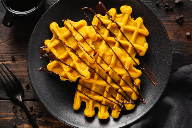 Pumpkin waffles with chocolate and sugar powder on dark old background. Top view