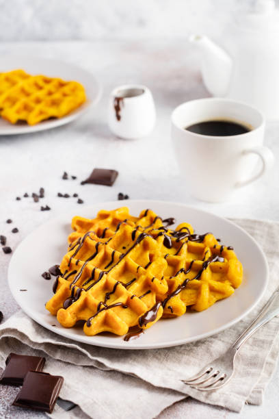 Pumpkin waffles with chocolate and icing sugar on light background and old rustic breakfast table. Top view.