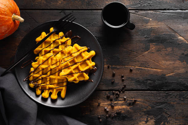 Pumpkin waffles with chocolate and sugar powder on dark old background. Top view