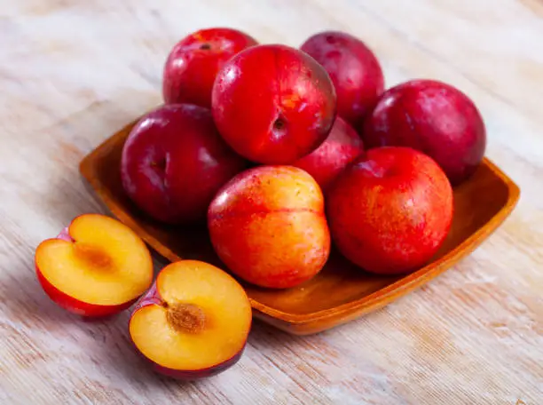 Photo of Ripe red plums in wooden bowl