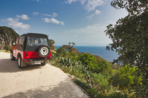 Malta - March 19 2020: A bright red jeep on a road on the edge of a cliff overlooking the sea