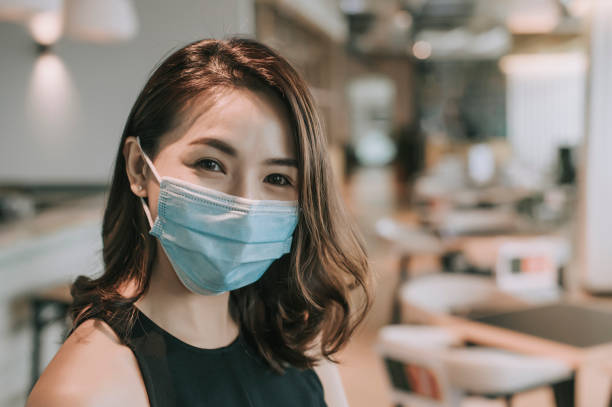 an asian chinese beautiful woman looking at camera smiling with her face mask surgical mask on an asian chinese beautiful woman looking at camera smiling with her face mask surgical mask on malaysia office workers stock pictures, royalty-free photos & images