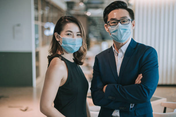 an asian chinese beautiful woman and handsome man looking at camera smiling with their face mask surgical mask on an asian chinese beautiful woman and handsome man looking at camera smiling with their face mask surgical mask on covid secure photos stock pictures, royalty-free photos & images