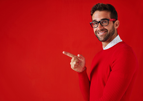 Studio portrait of a handsome and stylish young man pointing towards copyspace against a red background