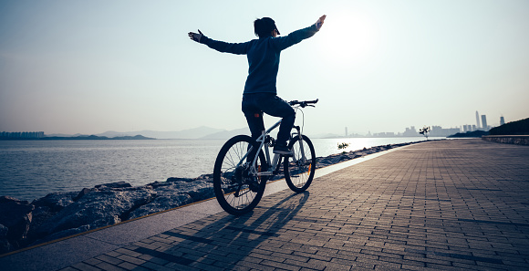 Female cyclist hands free cycling riding bike with arms outstretched in the coasts sunrise