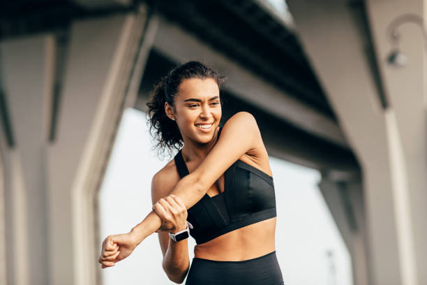 istock Woman athlete warming up her body before evening training under a highway. Smiling female stretching arm outdoors. 1225963350