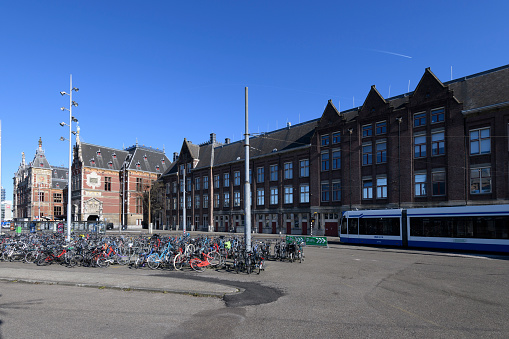 Bicycles in front of Amsterdam central railway station. A tram is passing and people are crossing the street in the background.
