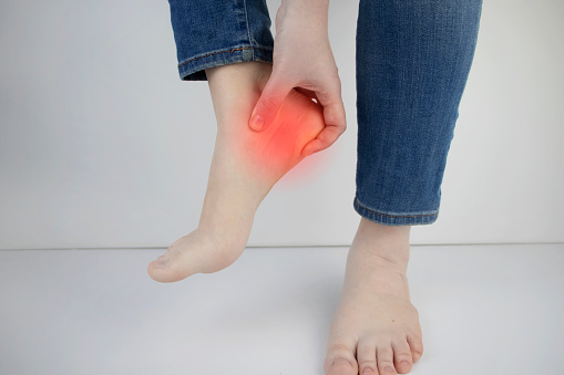 The concept of diseases and pains in the leg. Woman suffering from heel pain. Inflammation or sprain of the tendon in the foot, heel spur, bursitis.