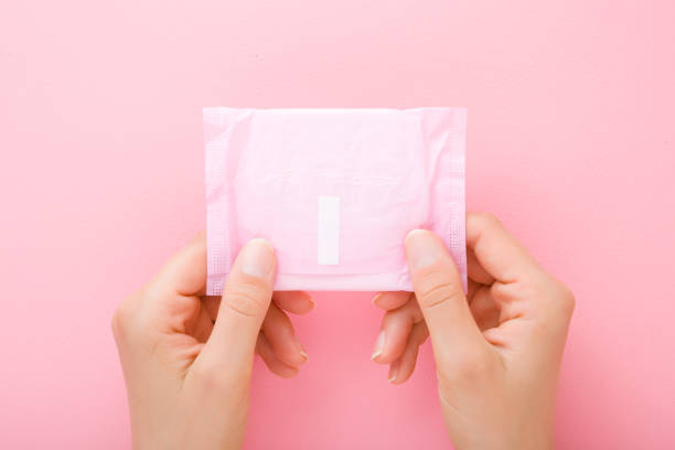 jeunes mains de femme retenant le paquet de serviette hygiénique sur le fond rose clair de table. couleur pastel. closeup. tir de point de vue. vue en haut vers le bas. - sanitary photos et images de collection