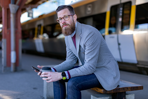 A man with a smart phone and reusable coffee mug on a railway station