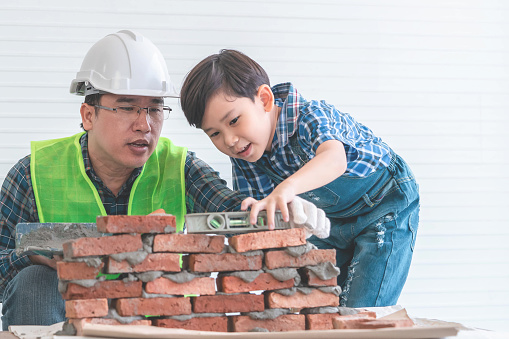 Little boy is learning how to lay down brick work from his builder father in vintage tone