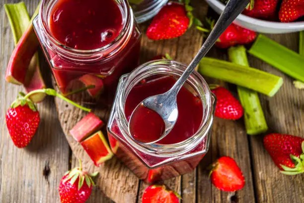 Homemade strawberry rhubarb jam or sauce, with fresh rhubarb and strawberries and spices, wooden rustic background copy space