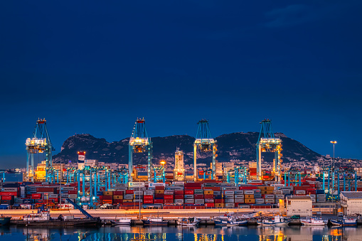 Algeciras, Cádiz, Spain - May 19, 2020: Night view of the commercial port of Algeciras, full of containers and huge cranes. In the background the rock of Gibraltar.