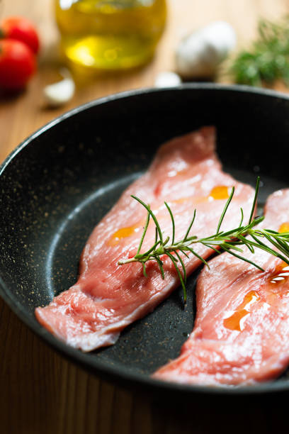 Raw Veal Meat Steaks on a pan, tomatoes, rosemary, oil, garlic. Wooden background, side view stock photo