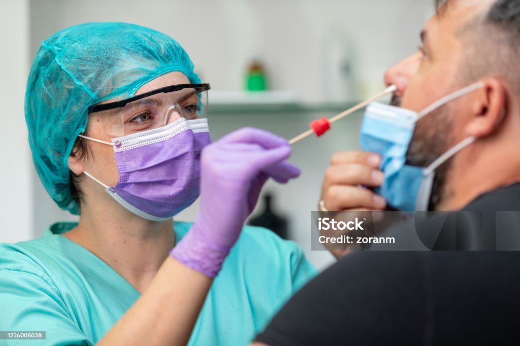 Female doctor in protective workwear taking nose swab test from mid adult man Female doctor in protective workwear taking nose swab test from middle aged man wearing protective face mask, Covid-19 pandemic outbreak Coronavirus Stock Photo