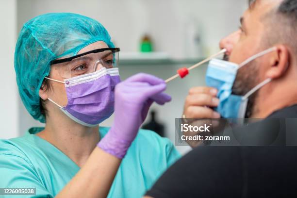 Female Doctor In Protective Workwear Taking Nose Swab Test From Mid Adult Man Stock Photo - Download Image Now