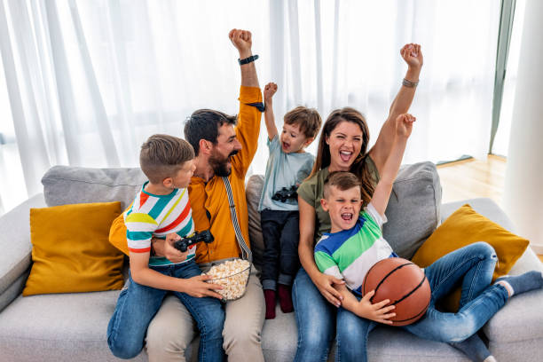smiling family sitting on the couch together playing video games - gamer watching tv adult couple imagens e fotografias de stock