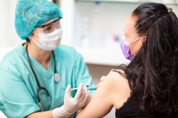 female doctor in protective workwear injecting vaccine and monitoring patient - syringe healthcare and medicine vaccination nurse imagens e fotografias de stock