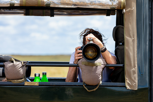 Female professional photographer on safari. Woman rests camera on a bean bag and shoots wildlife from a safari vehicle.  in the Masai Mara, Kenya.