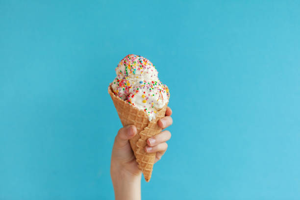 istock Children's hand holds delicious vanilla ice cream cone on a blue background. 1226009389
