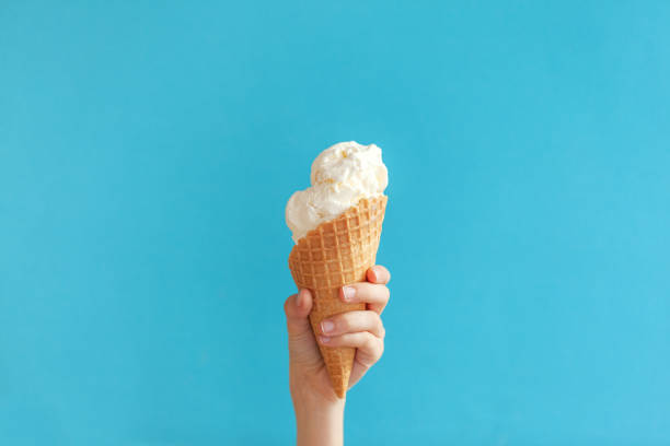 istock Children's hand holds delicious vanilla ice cream cone on a blue background. 1226009505