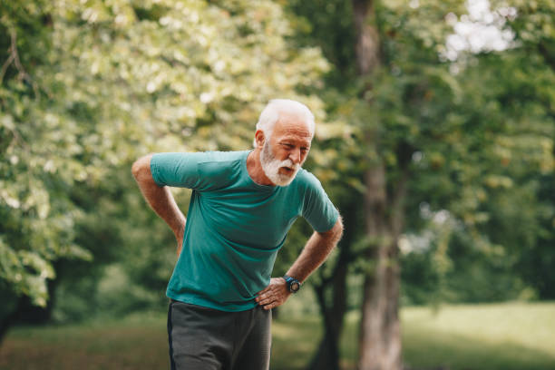 Sporty senior man having back pain while jogging. stock photo